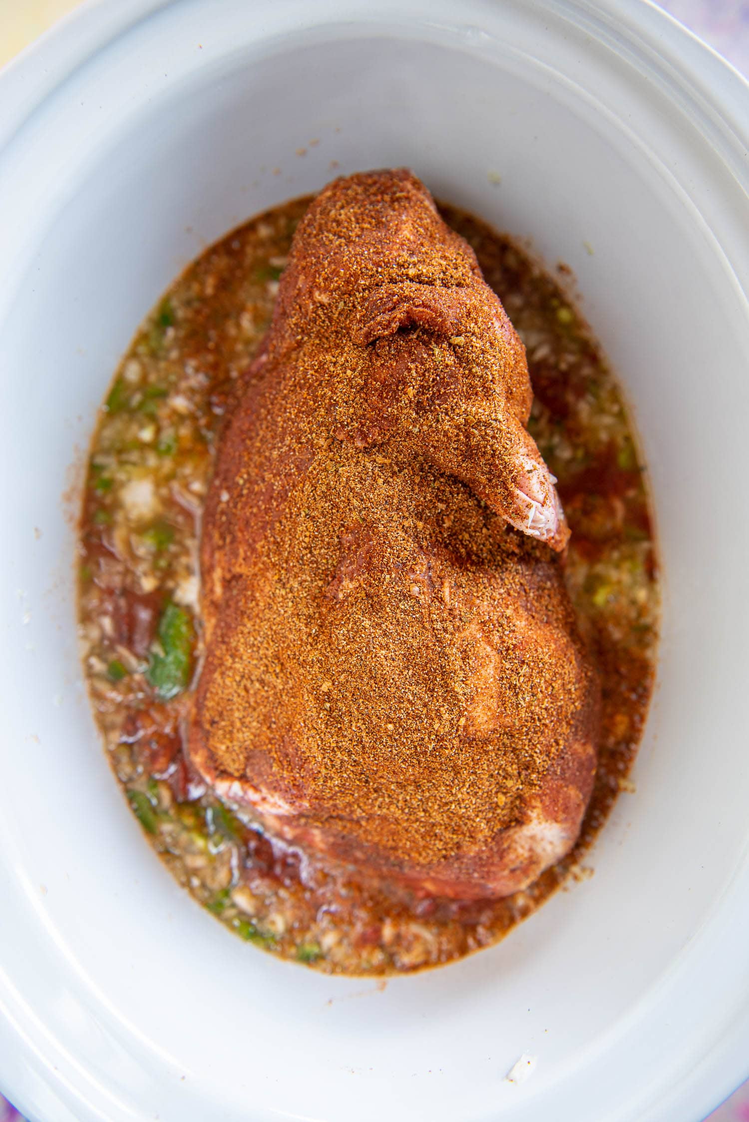 seasoned pork shoulder in white slow cooker ready to cook