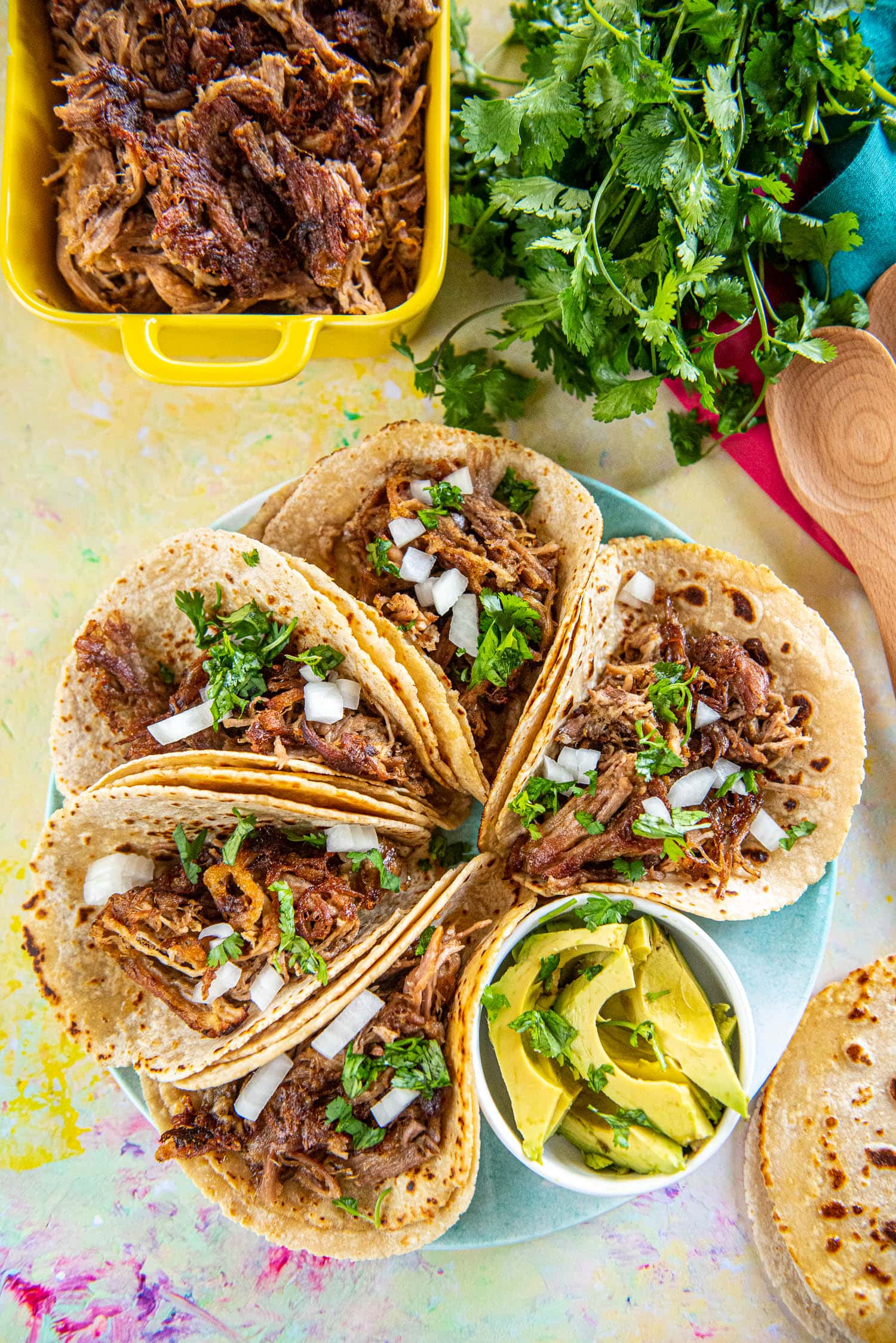 carnitas street tacos on a round blue plate with sliced avocados in a white dish