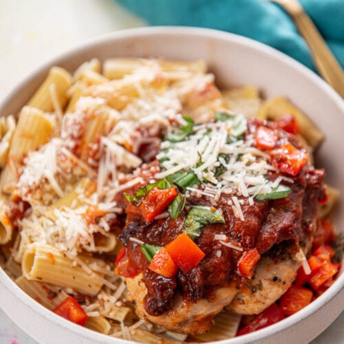 shallow pink bowl with pasta and topped with Italian chicken breasts and cheese