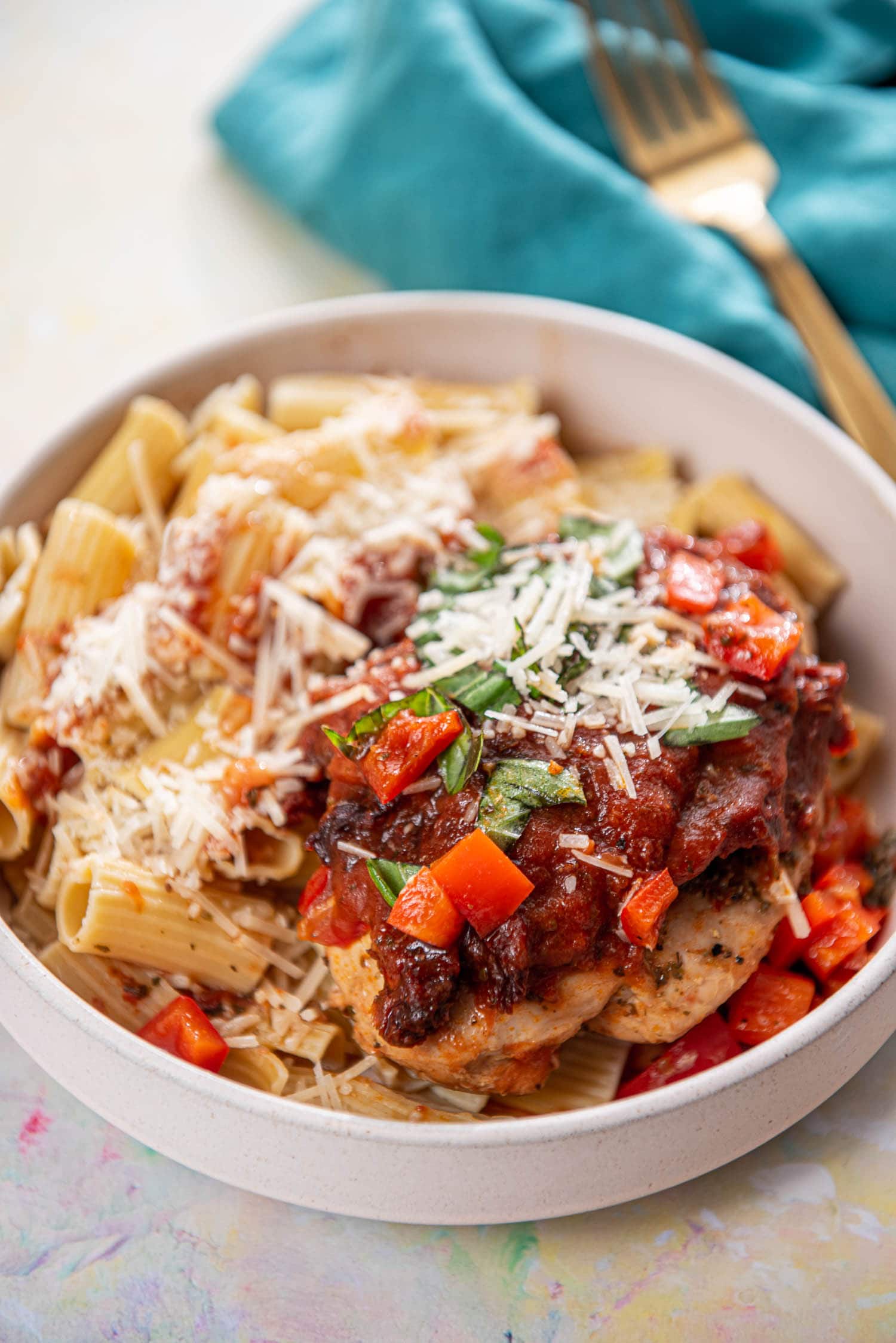 shallow pink bowl with pasta and topped with Italian chicken breasts and cheese