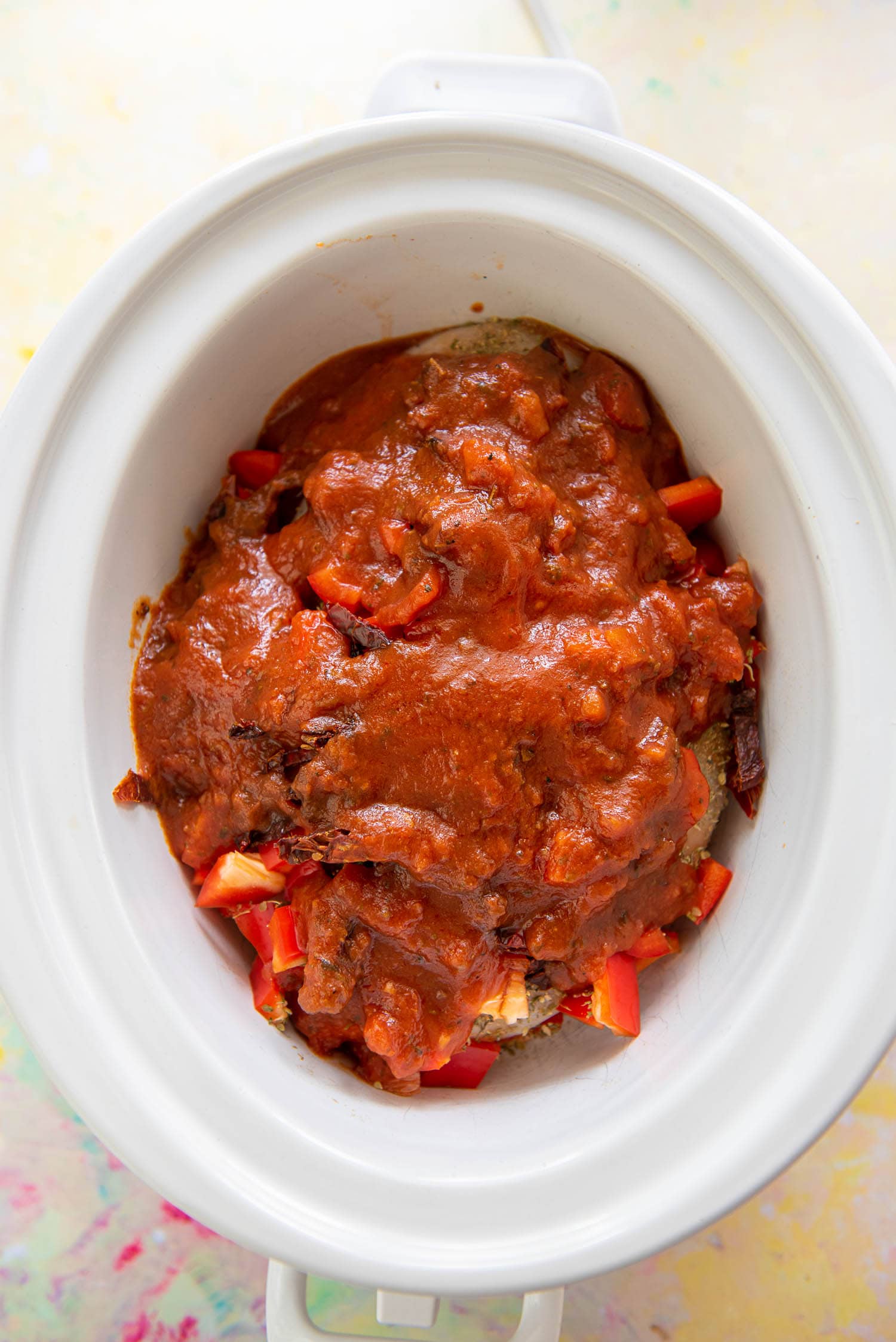 slow cooker with chicken breasts, peppers and sun dried tomatoes topped with marinara ready to cook