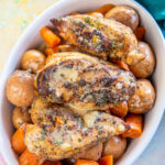 white oval serving dish layered with whole baby potatoes, cooked carrots, and topped with chicken breasts