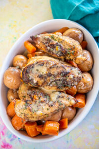 white oval serving dish layered with whole baby potatoes, cooked carrots, and topped with chicken breasts