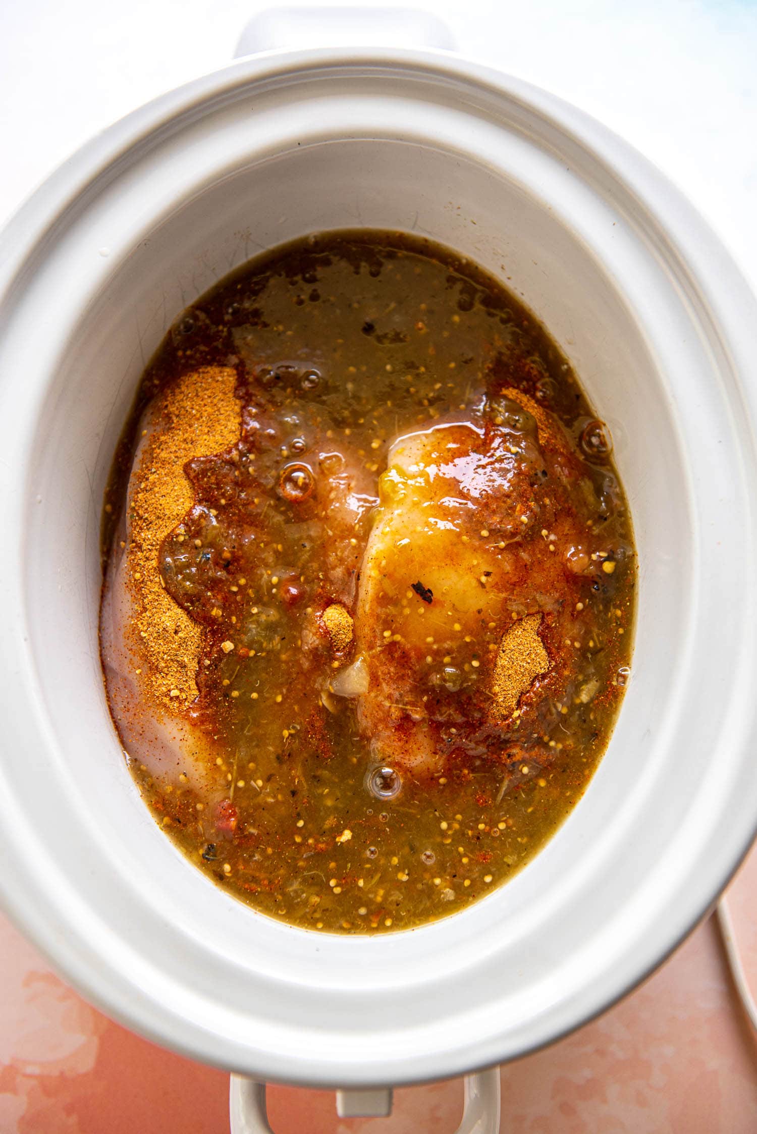 chicken breasts topped with seasoning and salsa in slow cooker