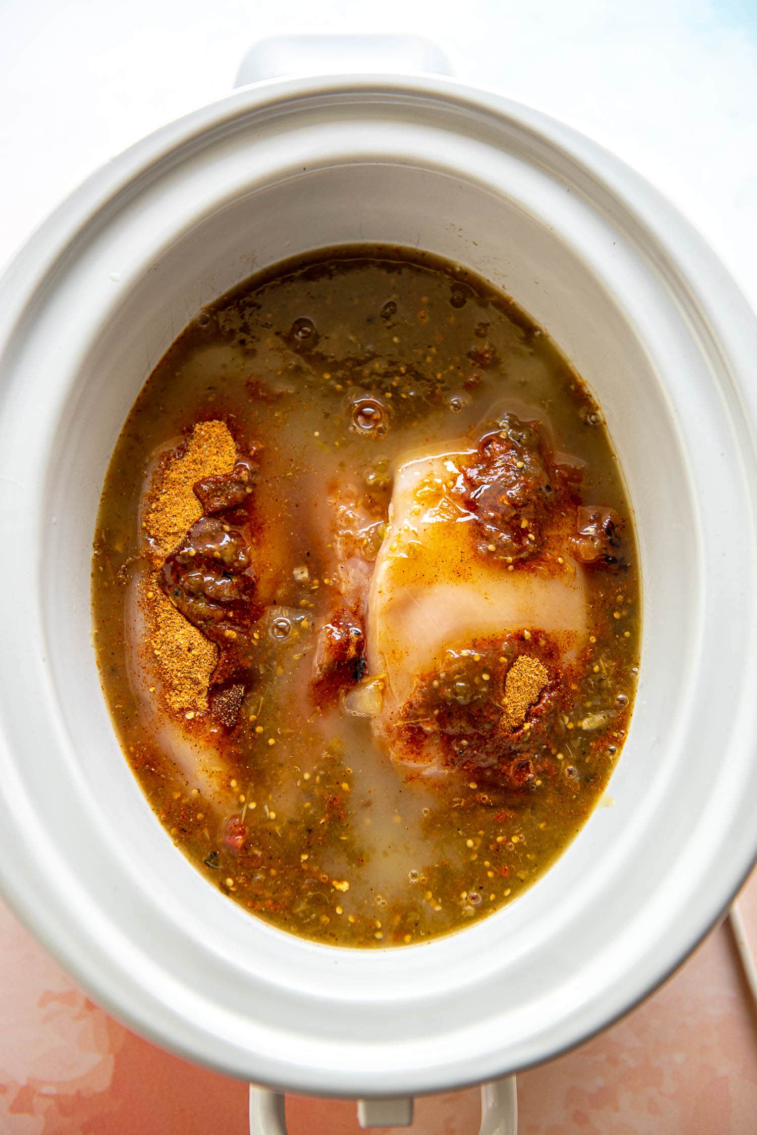 chicken ready to cook in slow cooker with salsa, broth and seasoning