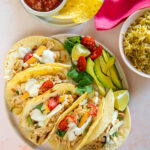 platter of chicken tacos next to bowl of rice and plate of chips and salsa