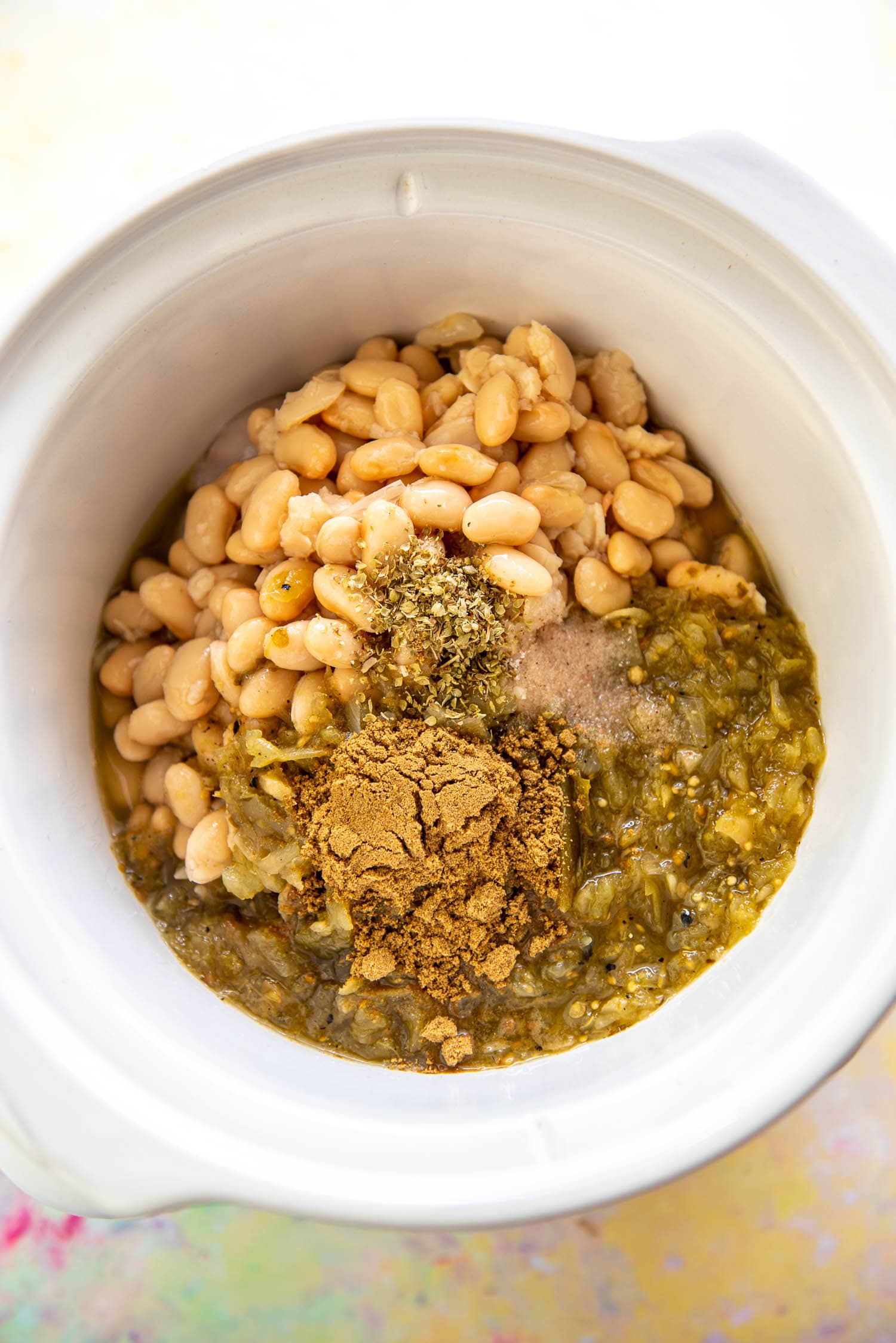 slow cooker filled with green salsa, white beans and seasoning