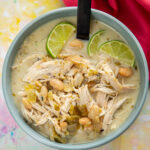 blue bowl filled with shredded chicken in white chicken chili topped with sliced limes