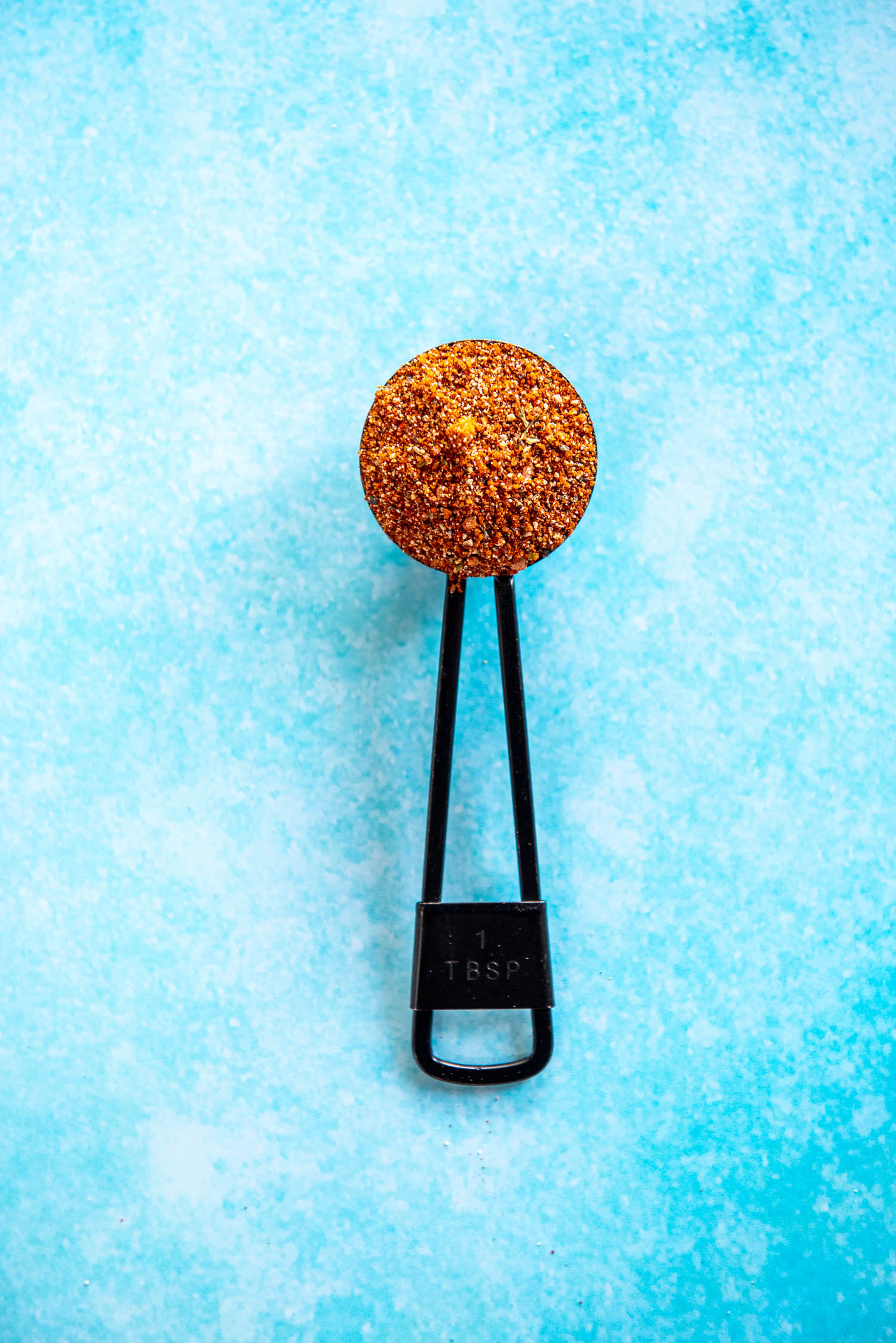 tablespoon filled with bbq rub seasoning on blue background
