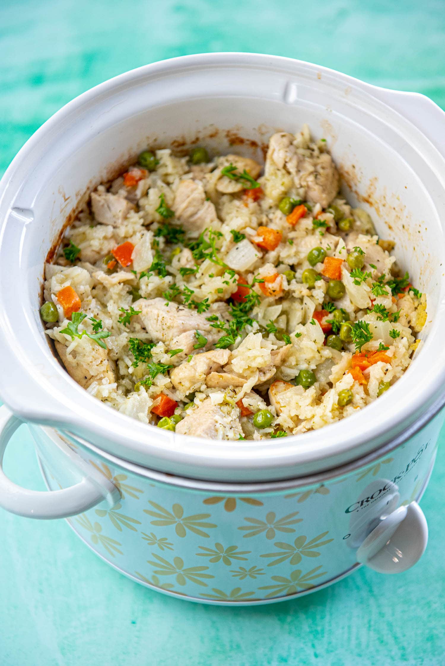 slow cooker with yellow flowers filled with chicken and rice casserole with peas and carrots