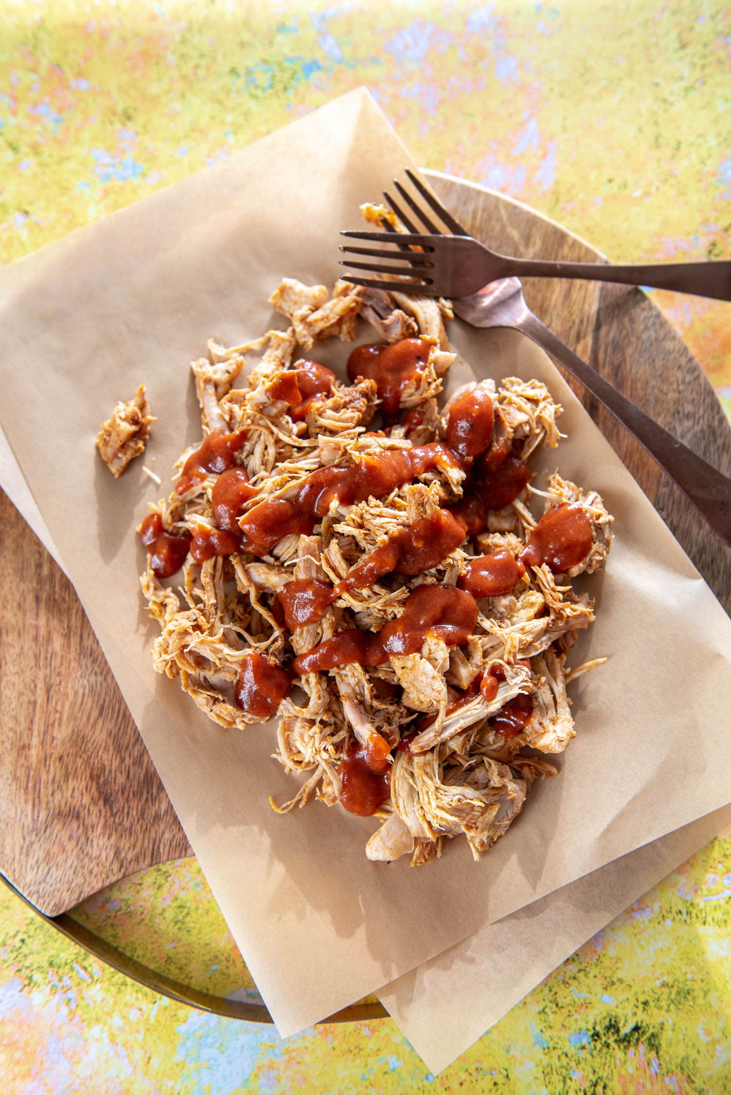 round wood board with shredded chicken topped with bbq sauce on parchment paper