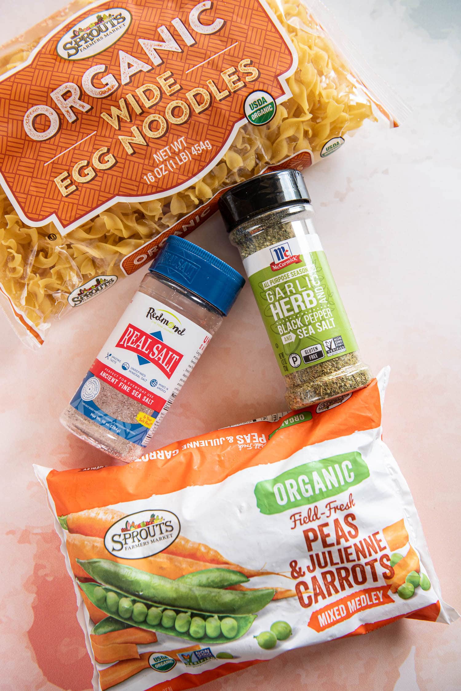 egg noodle package, bottle of real salt, bottle of garlic herb seasoning and bag of organic frozen peas and carrots