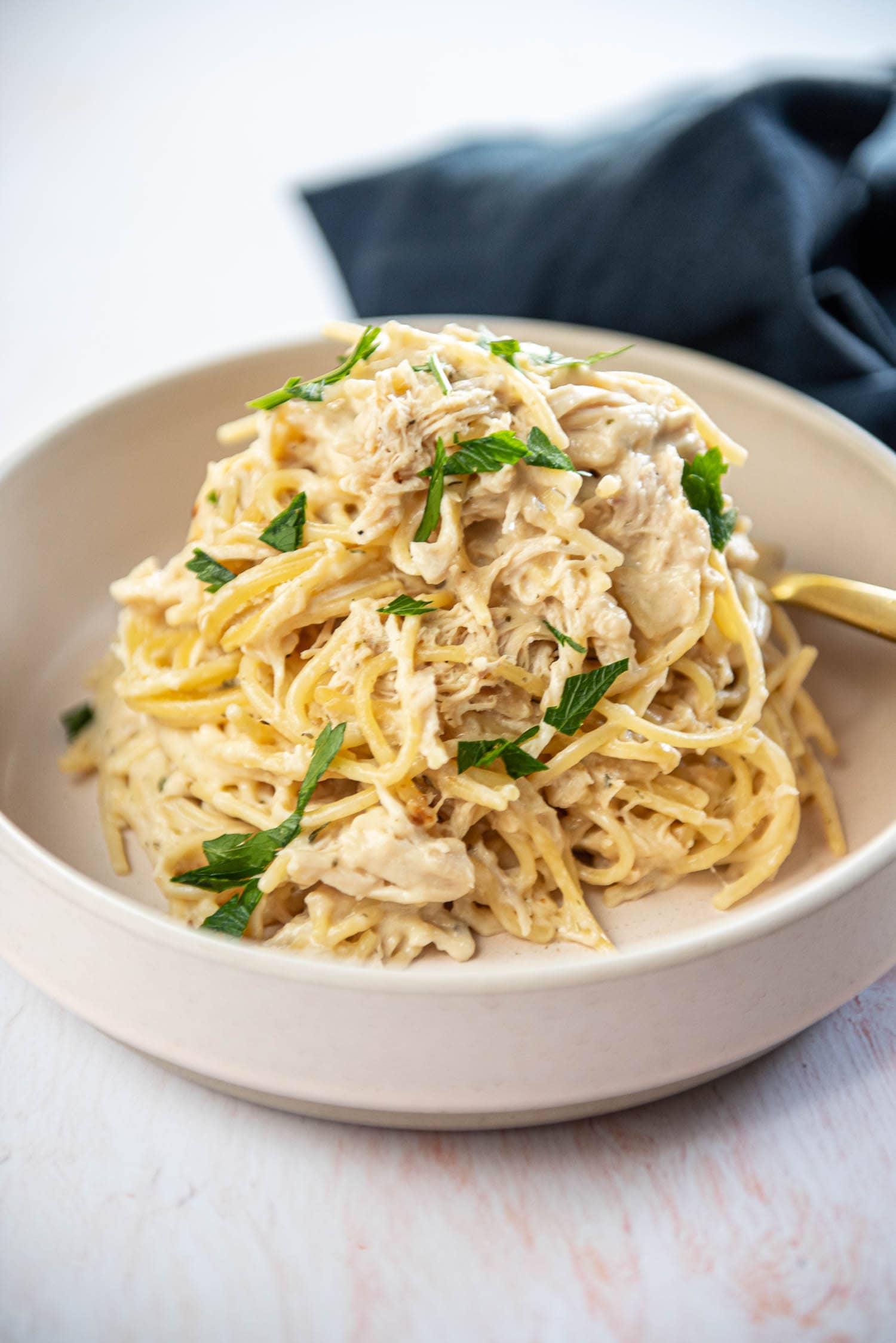 Cooked spaghetti mixed with white sauce, cooked chicken, and green garnishing in bowl on top table