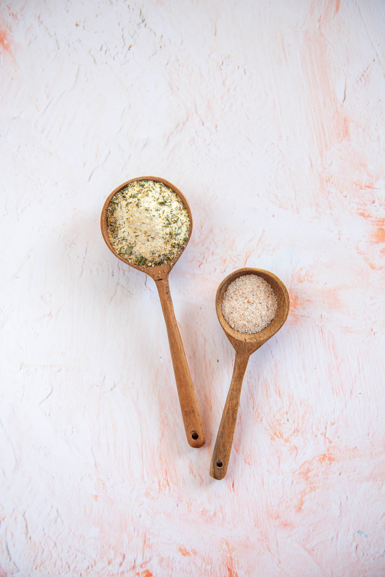 Two wooden spoons with spices inside on pink table