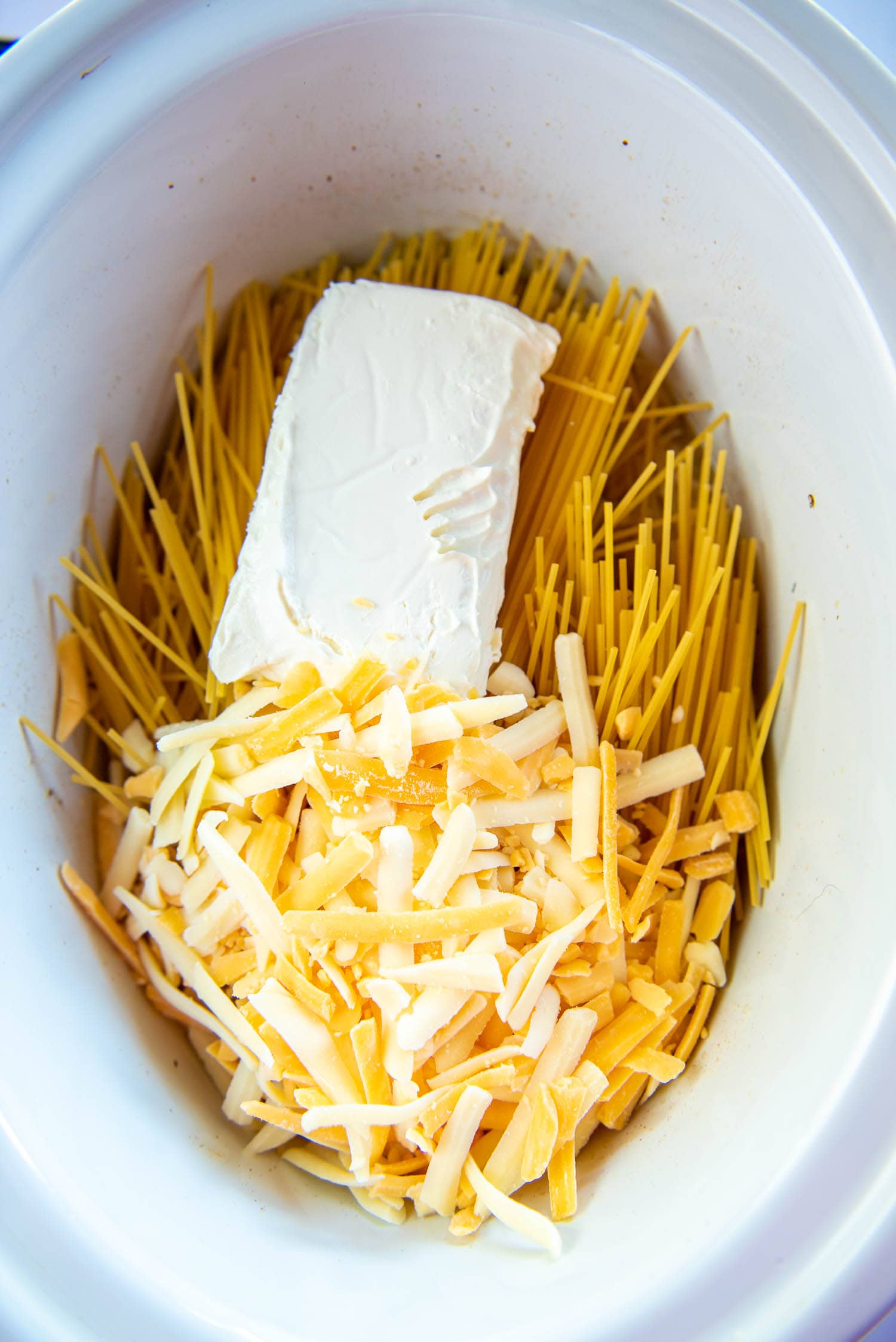 1lb spaghetti, triple cheddar blend cheese, and 8oz of cream cheese inside of white slow cooker bowl