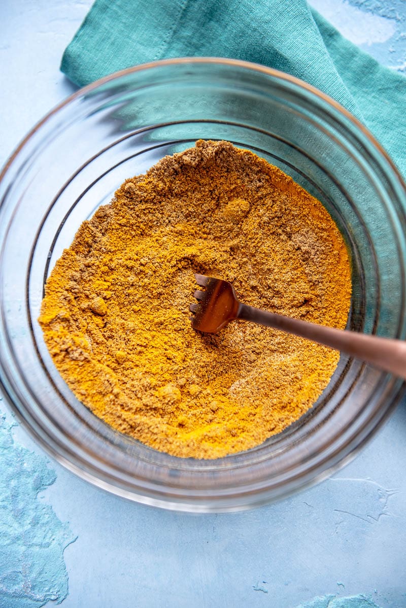 Seasonings and spices all mixed together with a fork inside of a glass bowl