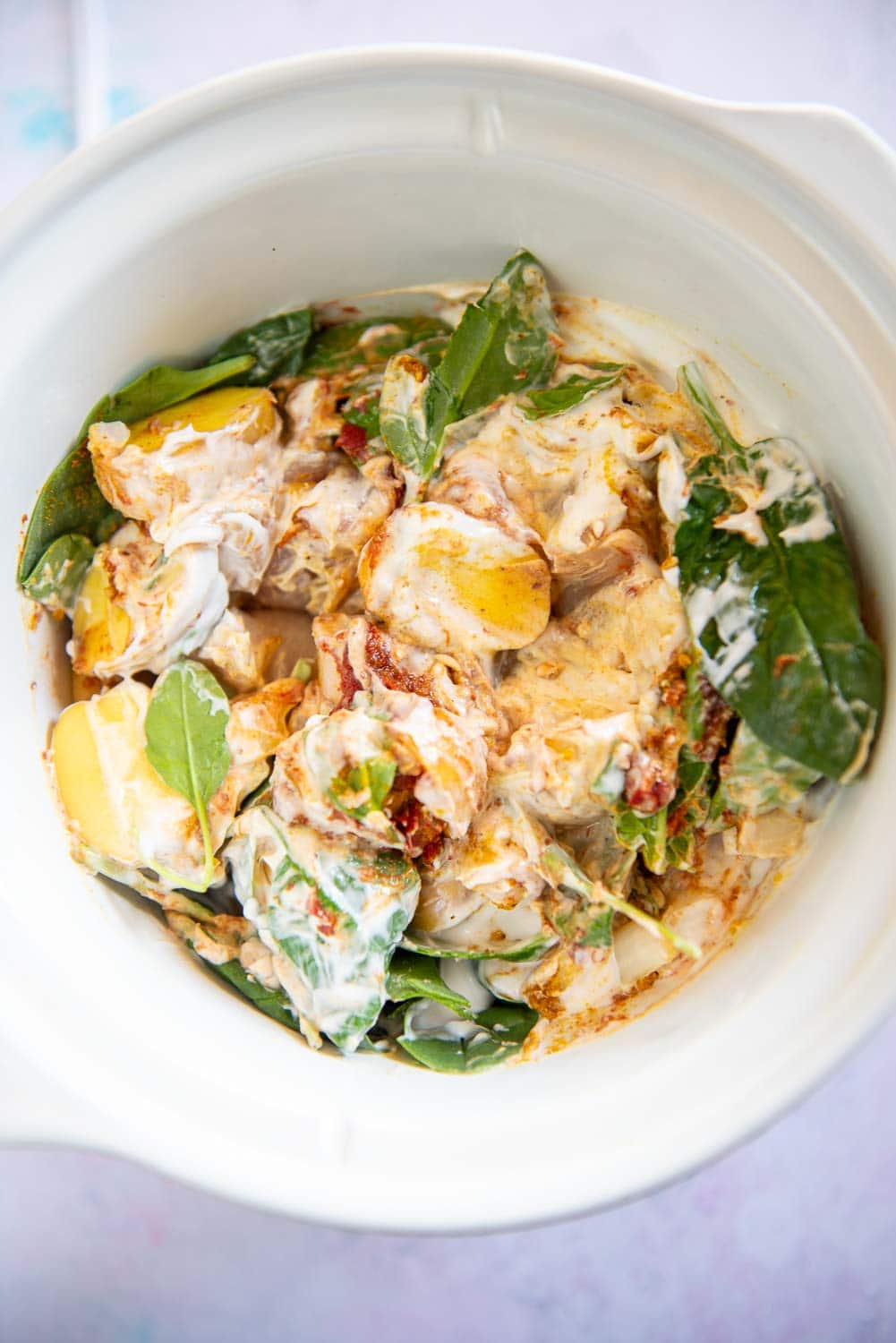 raw potatoes, spinach and chicken with seasonings mixed with coconut milk in slow cooker