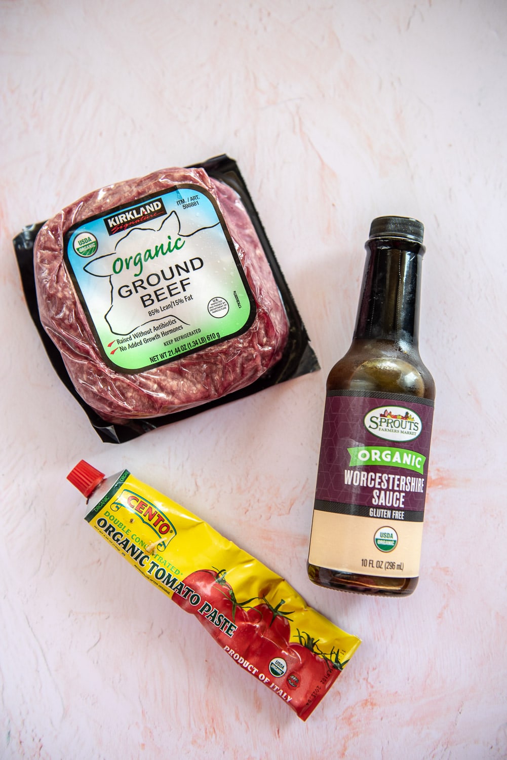 Pack of 1.34 lb ground beef, bottle of Worcestershire sauce, and tube of organic tomato paste with pink background
