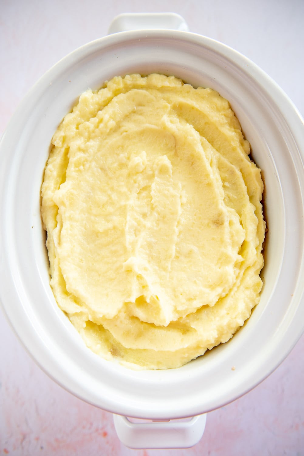 creamed mashed potatoes inside white slow cooker pot and pink background