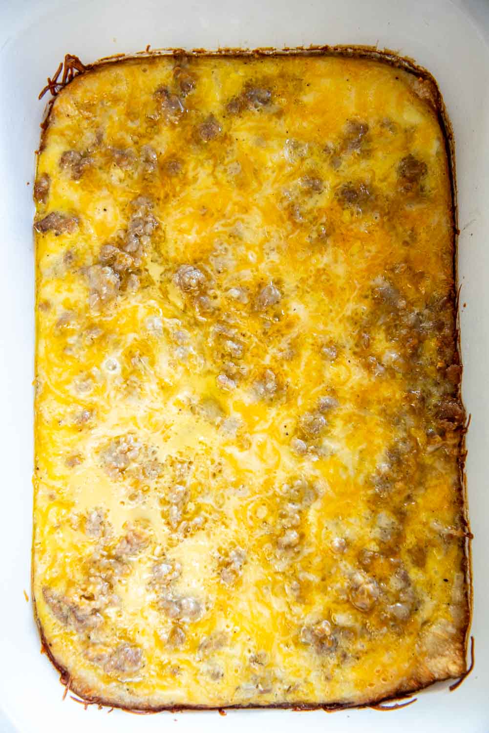 White baking dish with crescent rolls dough laid out and beaten eggs poured on top with ground pork breakfast sausage on top and shredded cheese on top cooked