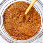 chili seasoning in a glass bowl with a wooden spoon inside