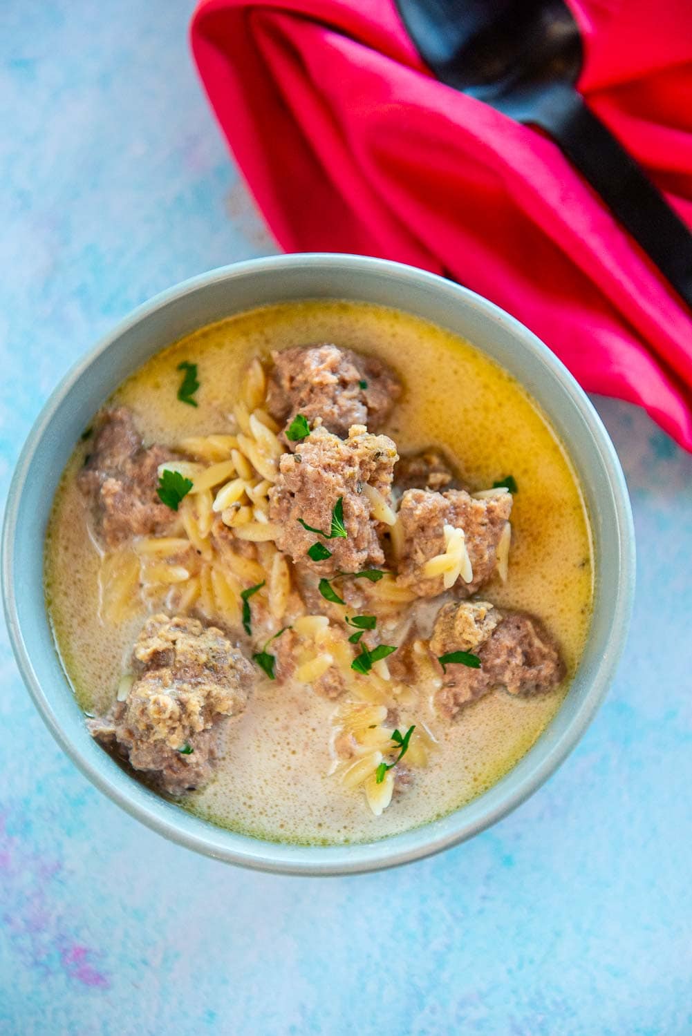 creamy meatball soup in the slow cooker served in a bowl on blue table next to spoon and red napkin