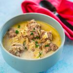 creamy meatball soup in the slow cooker served in a bowl on blue table next to spoon and red napkin