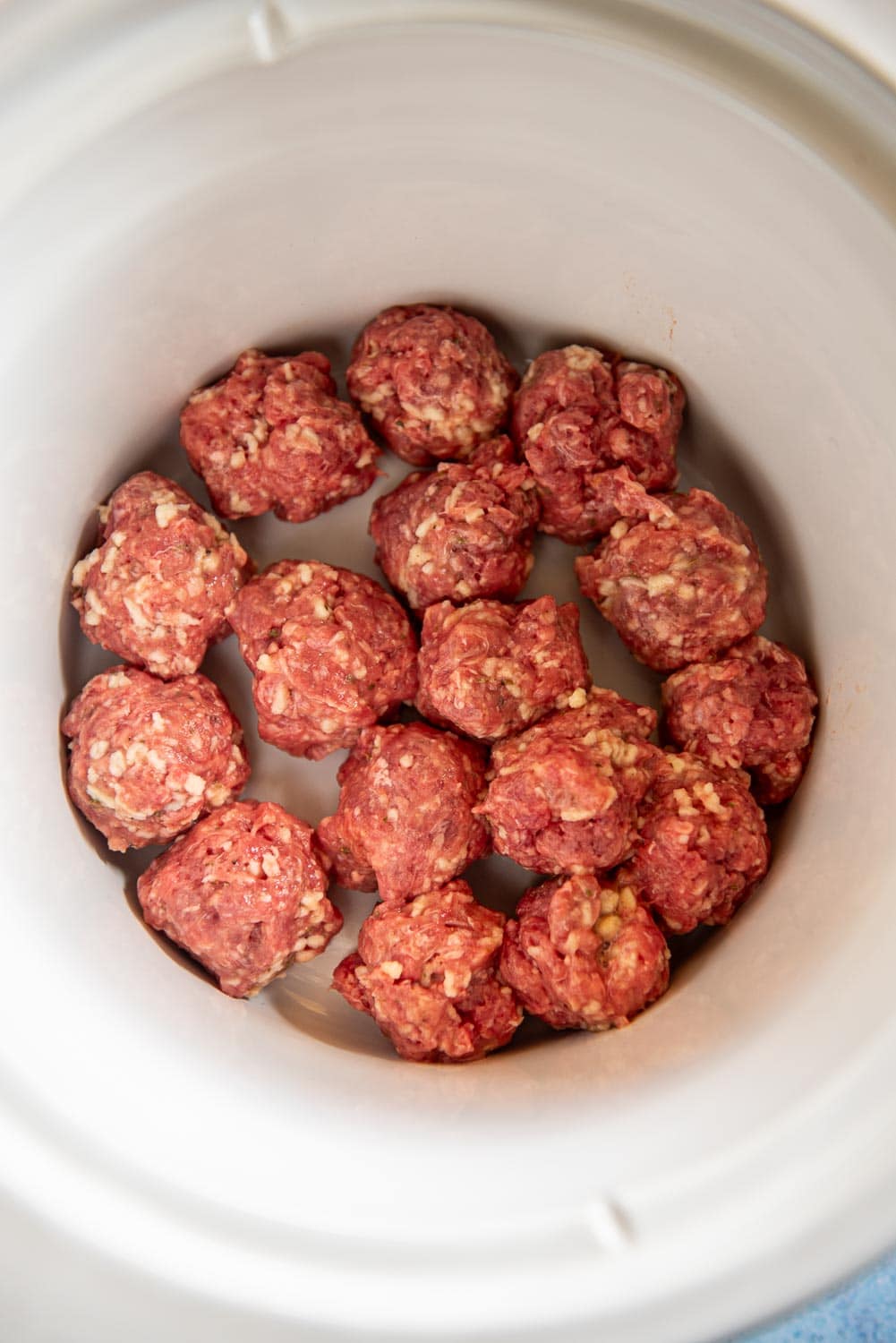 Raw quarter sized meatballs in a slow cooker white bowl