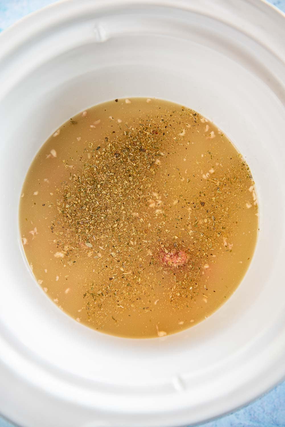 Seasonings and broth all inside a slow cooker bowl