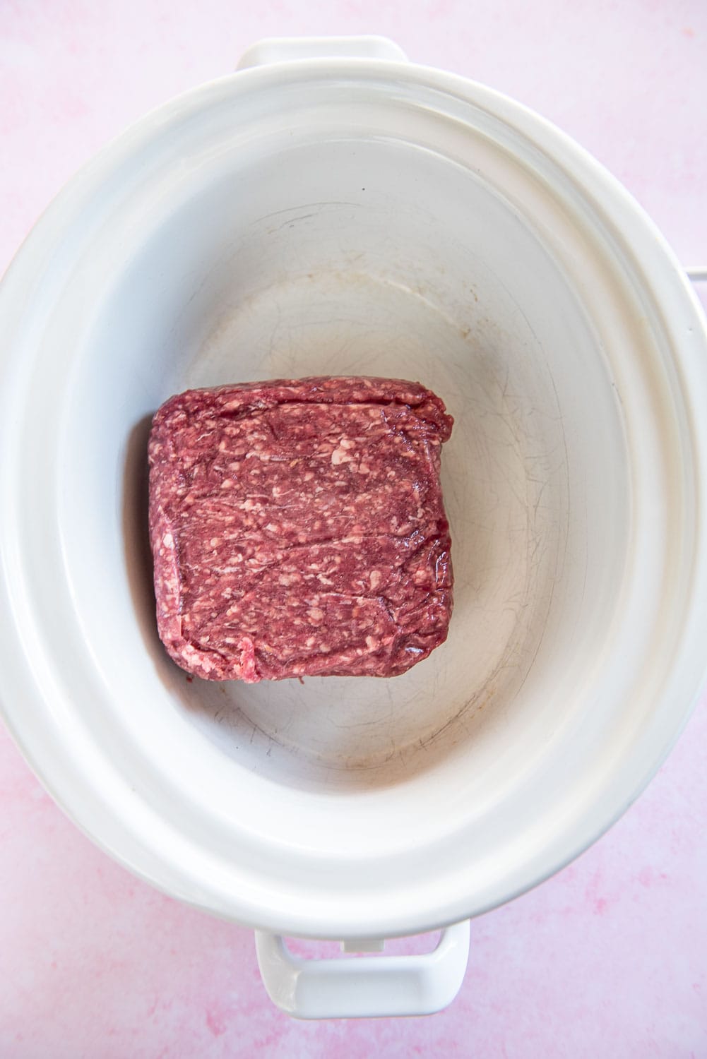 Raw pack of ground beef inside white slow cooker bowl