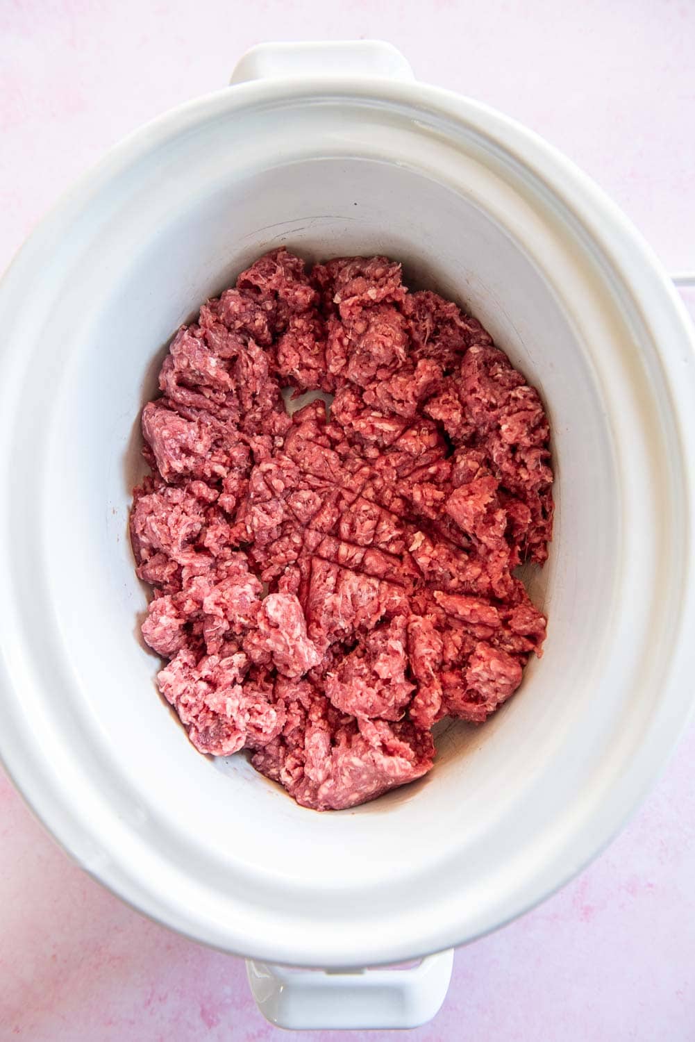raw ground beef broken apart inside of white slow cooker bowl