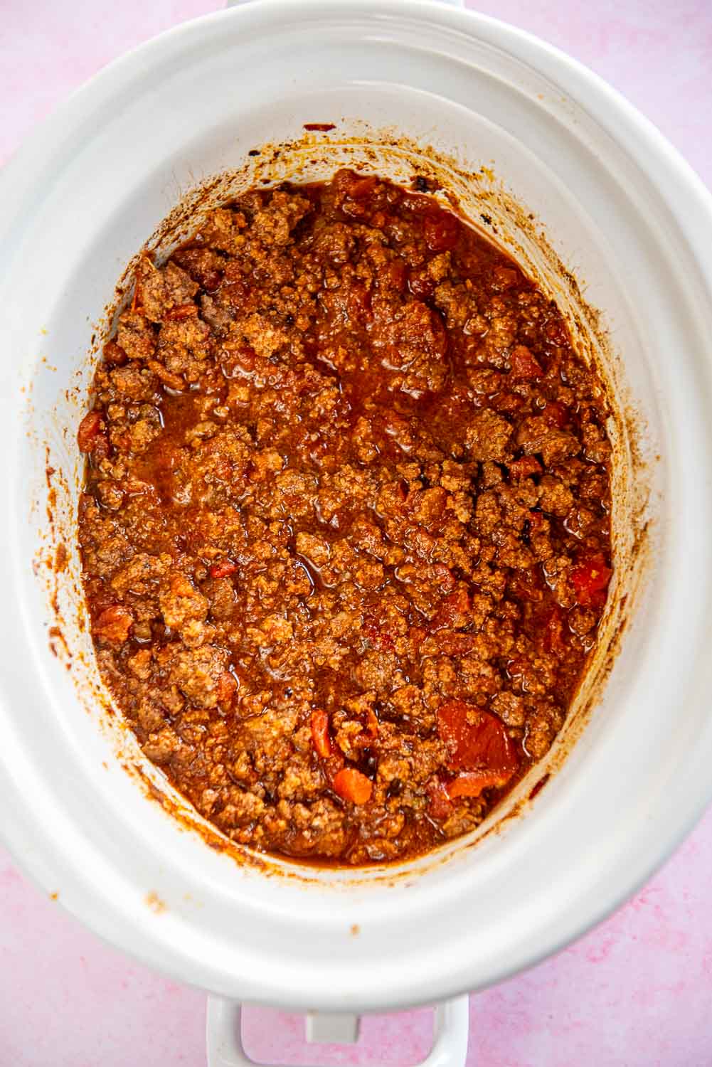Cooked taco meat in red sauce inside a white slow cooker bowl