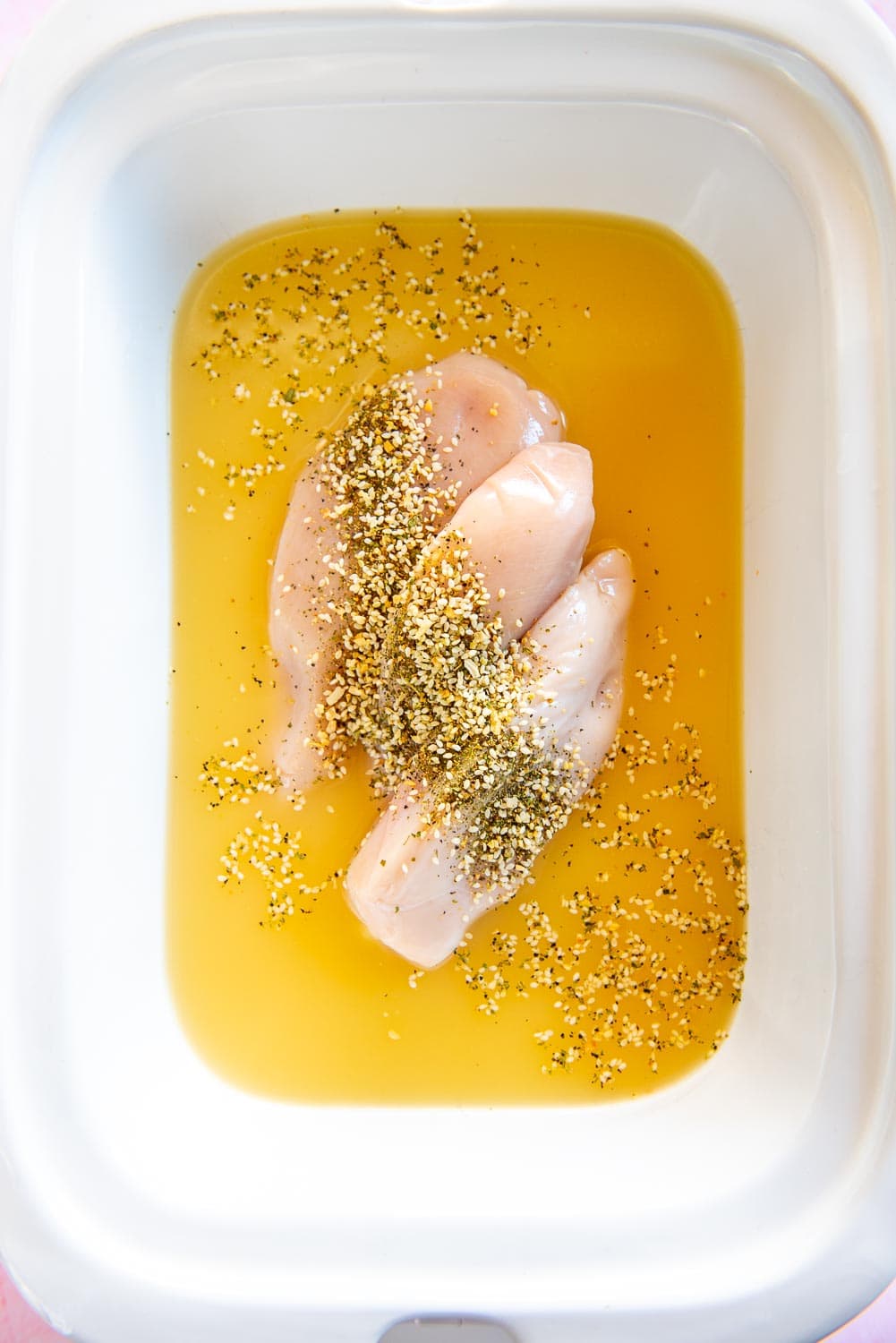 raw chicken breast in bone broth with seasonings and onions in white bowl