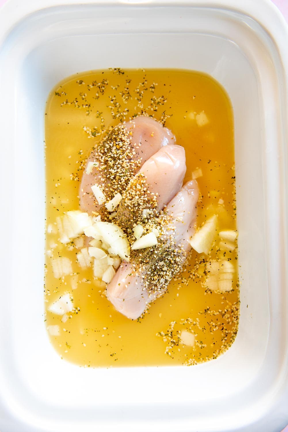 raw chicken breast in bone broth with seasonings and onions in white bowl