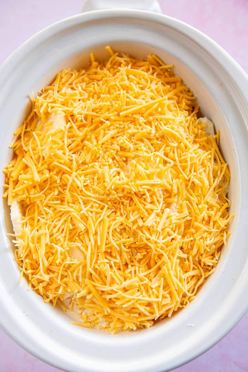 Slow cooker white bowl with potato mixture cheese thoroughly spread on top