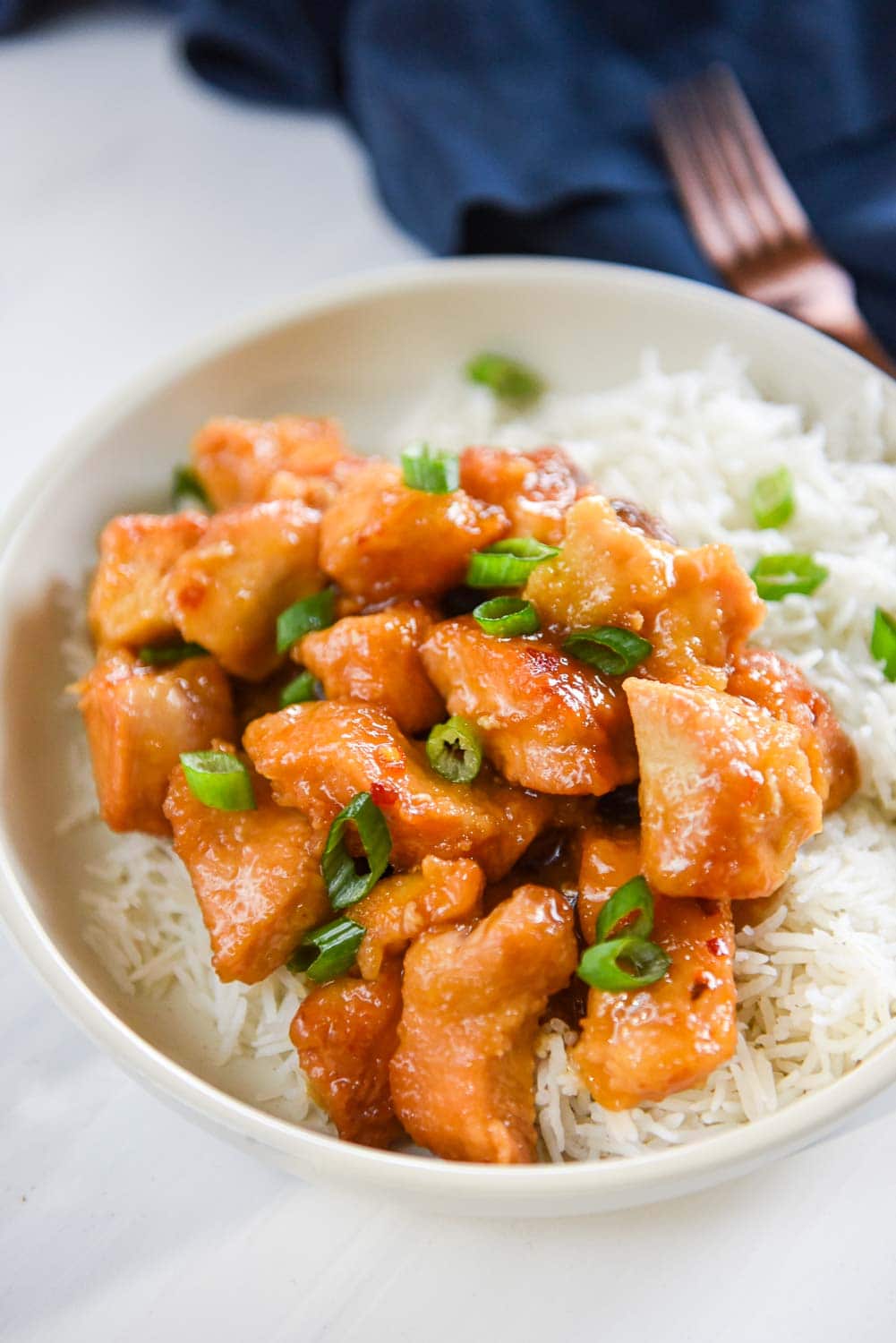 Orange chicken in white bowl with rice topped with chopped green onions