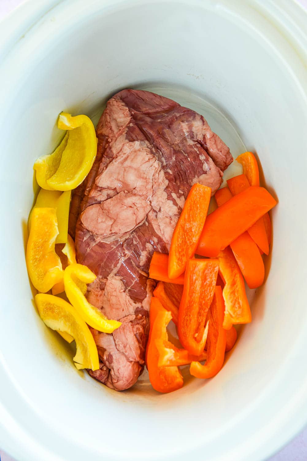 skirt steak and orange and yellow pepper slices in slow cooker