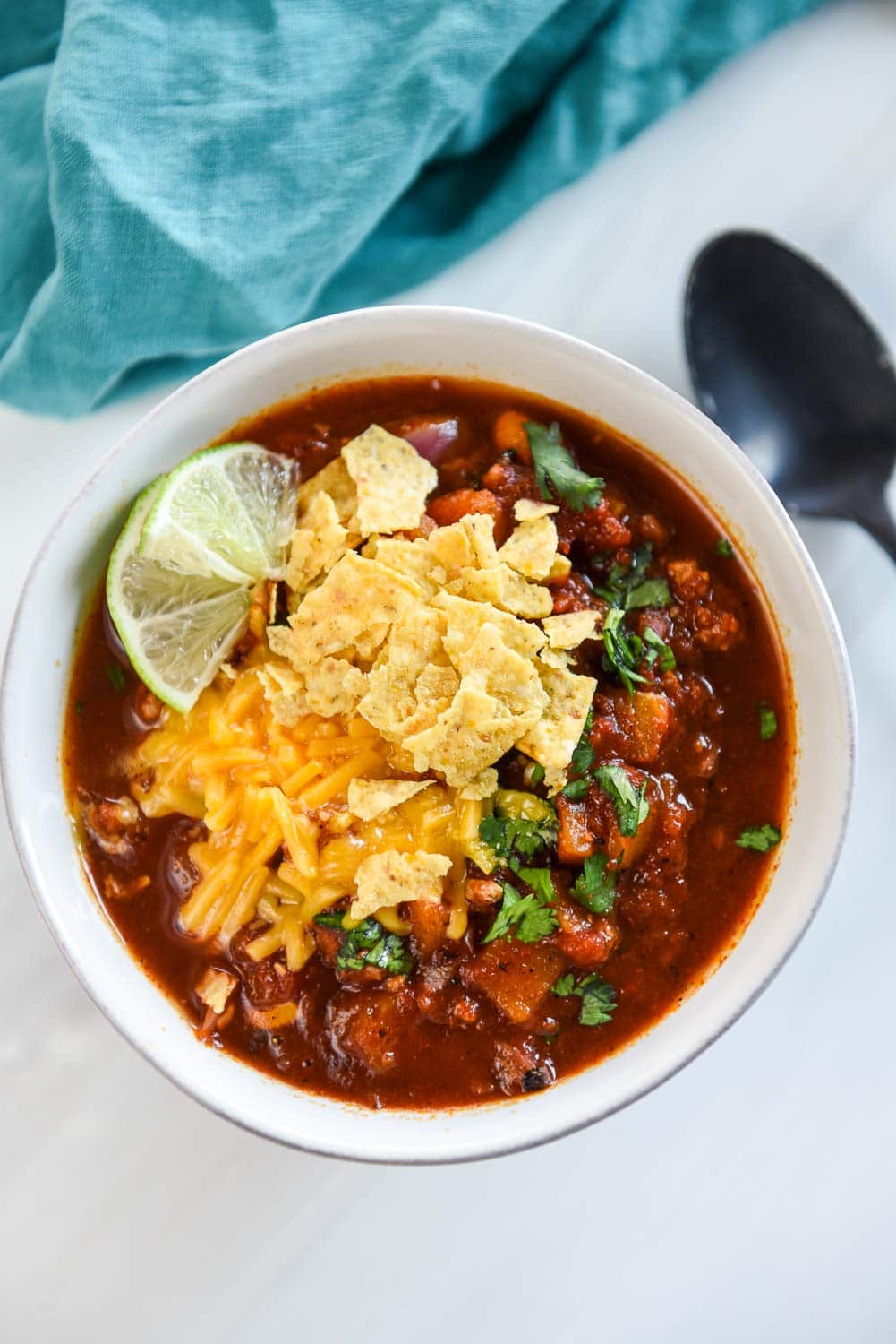 overhead view of bowl of turkey chili topped with sliced limes, shredded cheese and tortilla chips