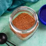 Glass jar with creole seasoning next to black tablespoon