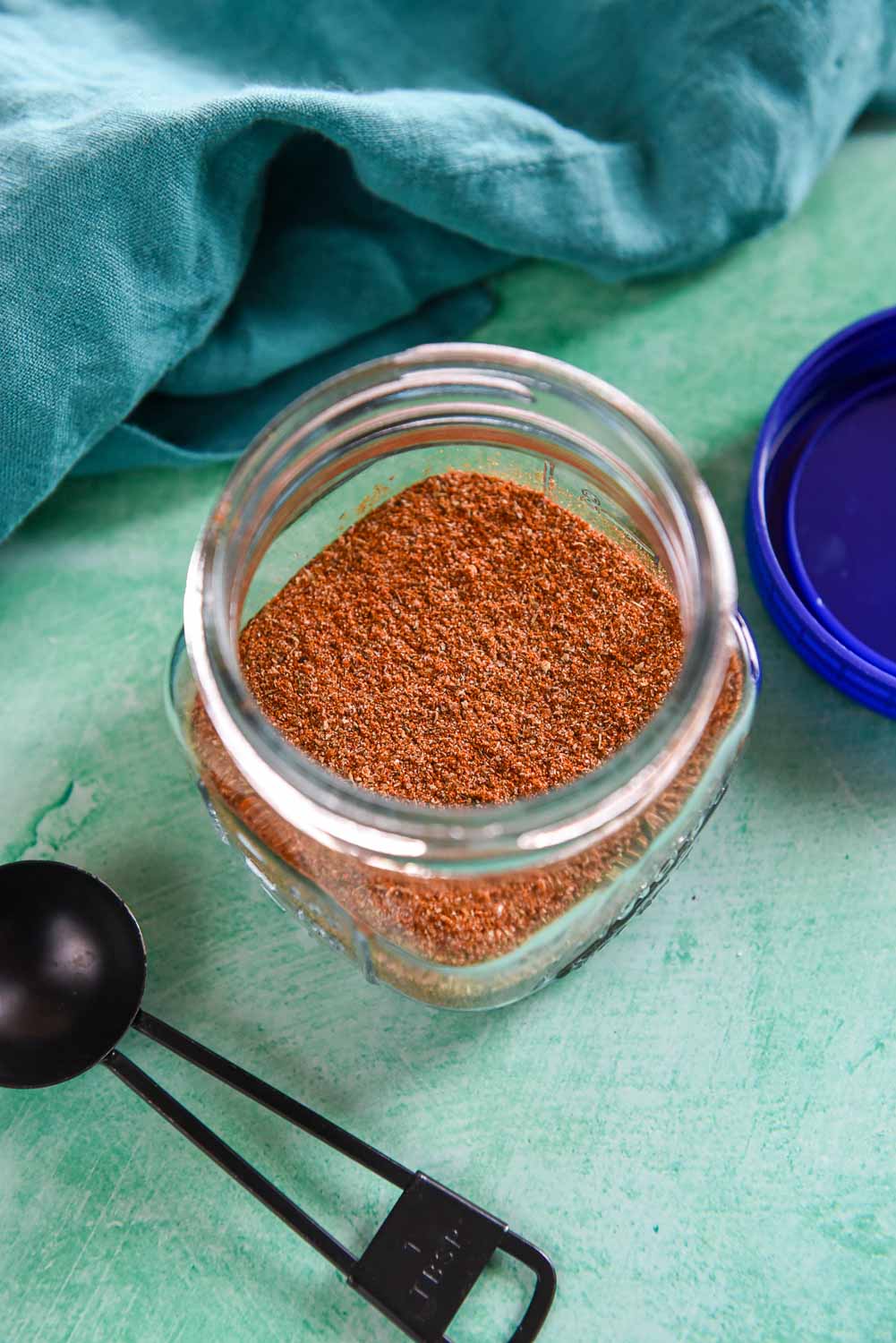 Glass jar with creole seasoning next to black tablespoon
