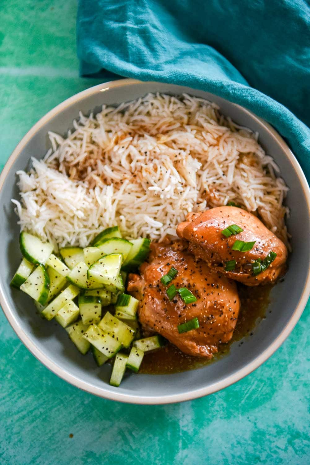 Bowls of adobo chicken, rice and marinated cucumbers