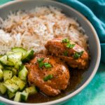 Chicken thighs with adobo sauce in bowl with rice and cucumbers