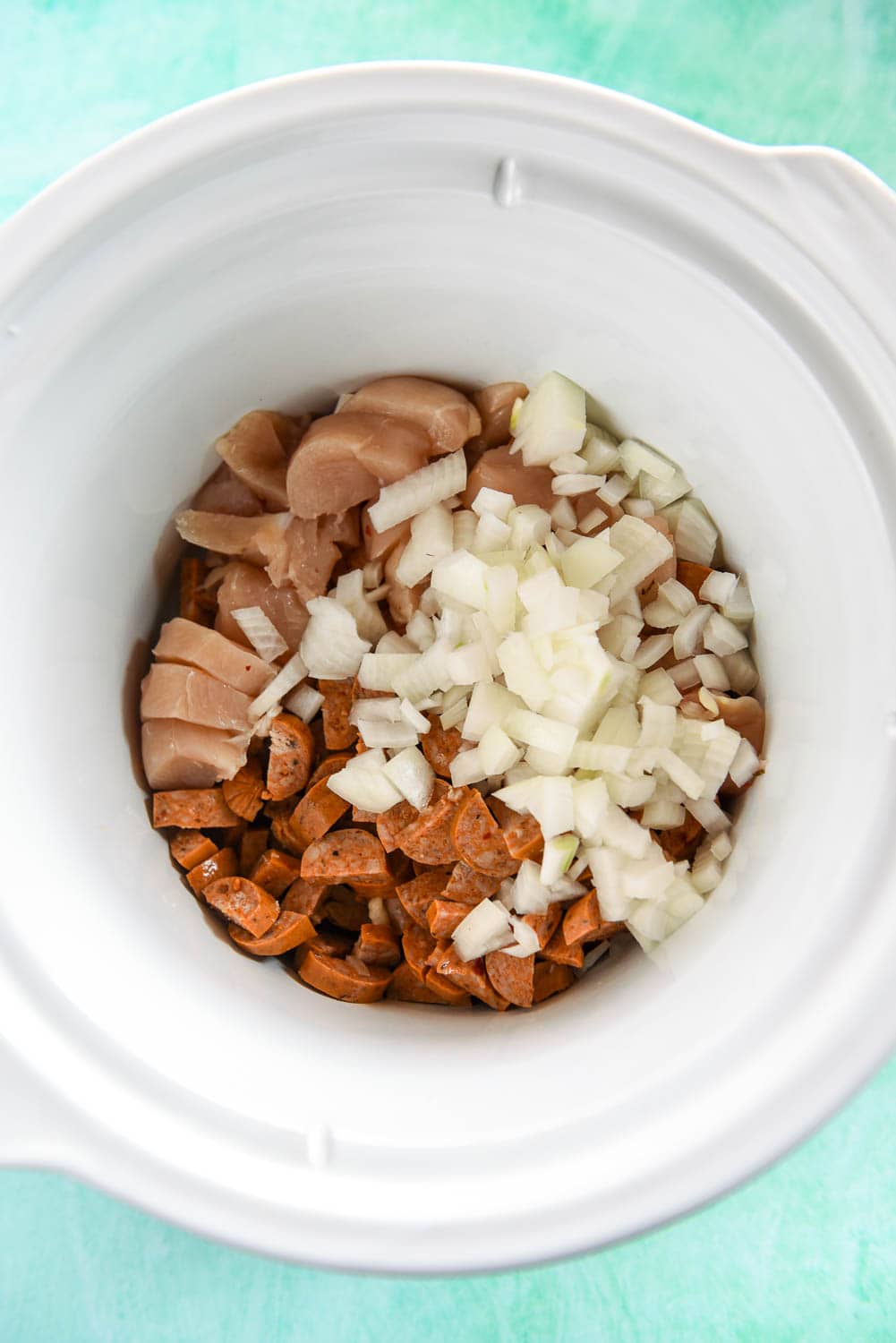 raw chicken, white onion and raw sausage chopped in white bowl
