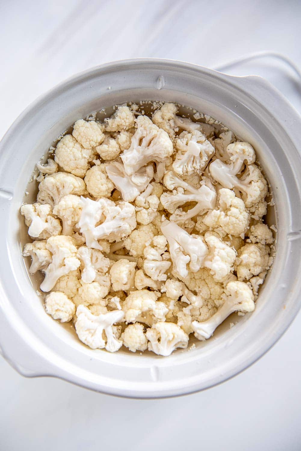 white slow cooker filled with fresh chopped cauliflower and water