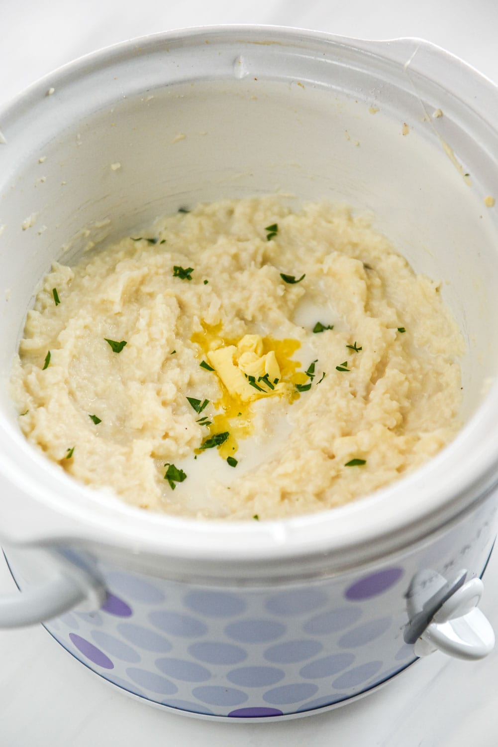 whipped cauliflower with dollop of melted butter in a purple dotted slow cooker