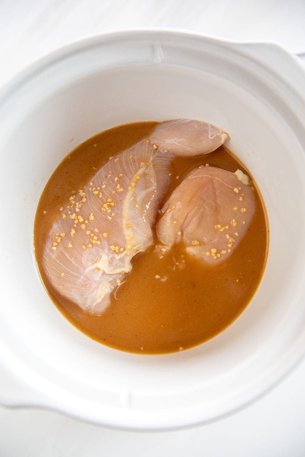 raw chicken breasts with sauce and garlic in slow cooker