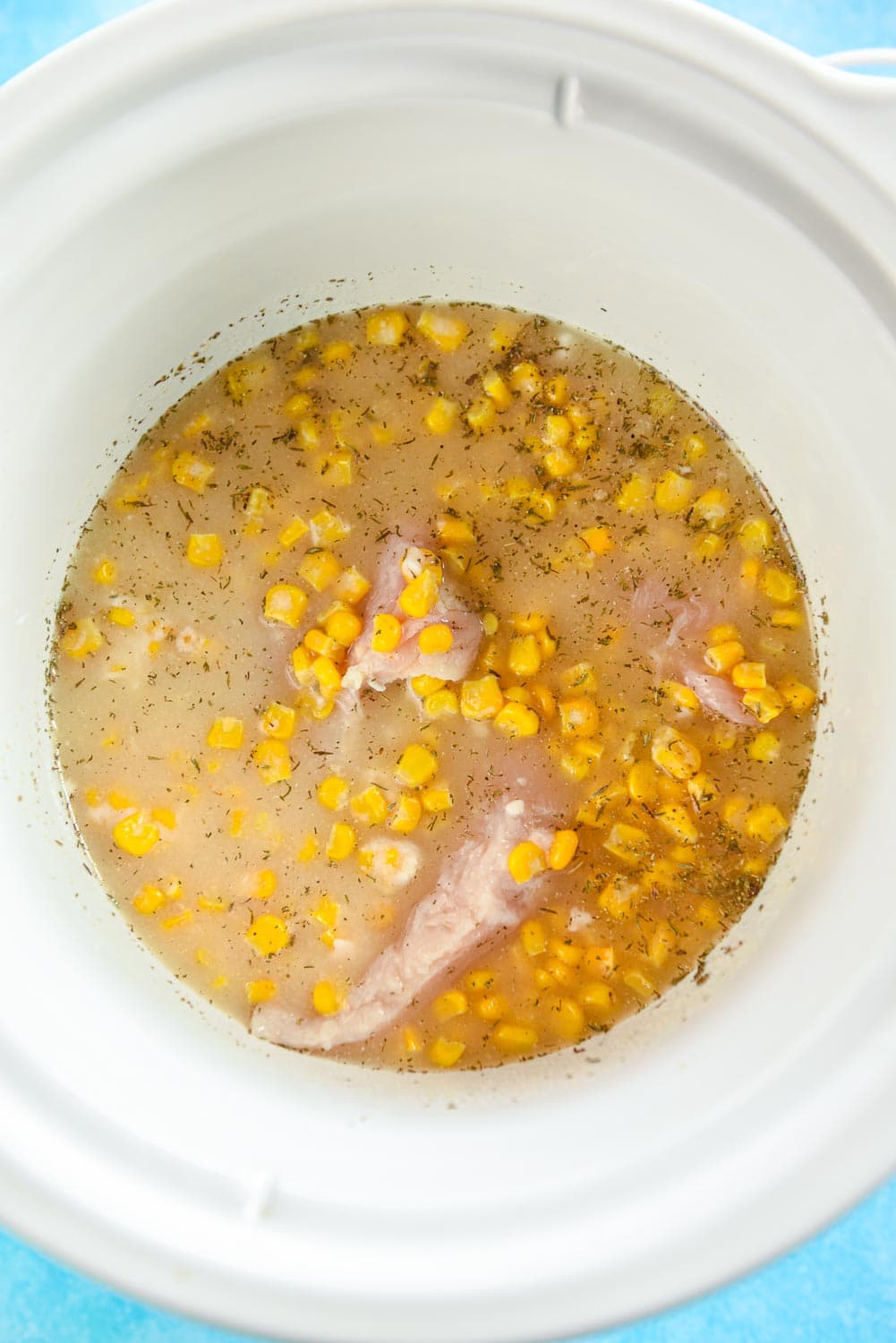 slow cooker with raw chicken, corn, spices and broth
