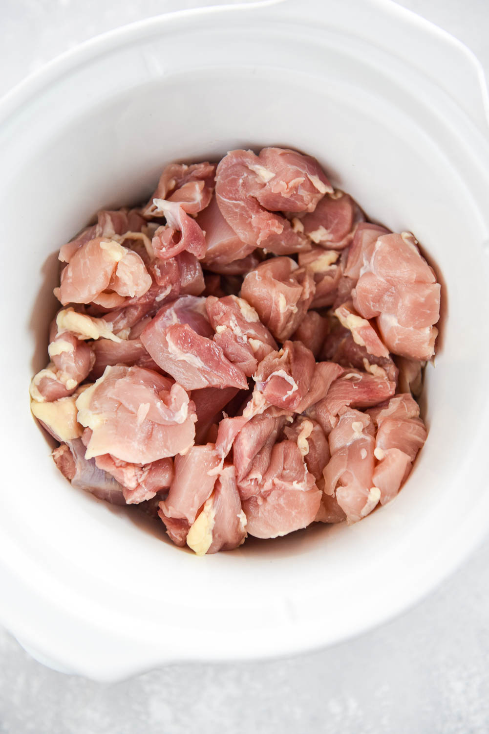 Raw chicken inside of white slow cooker bowl