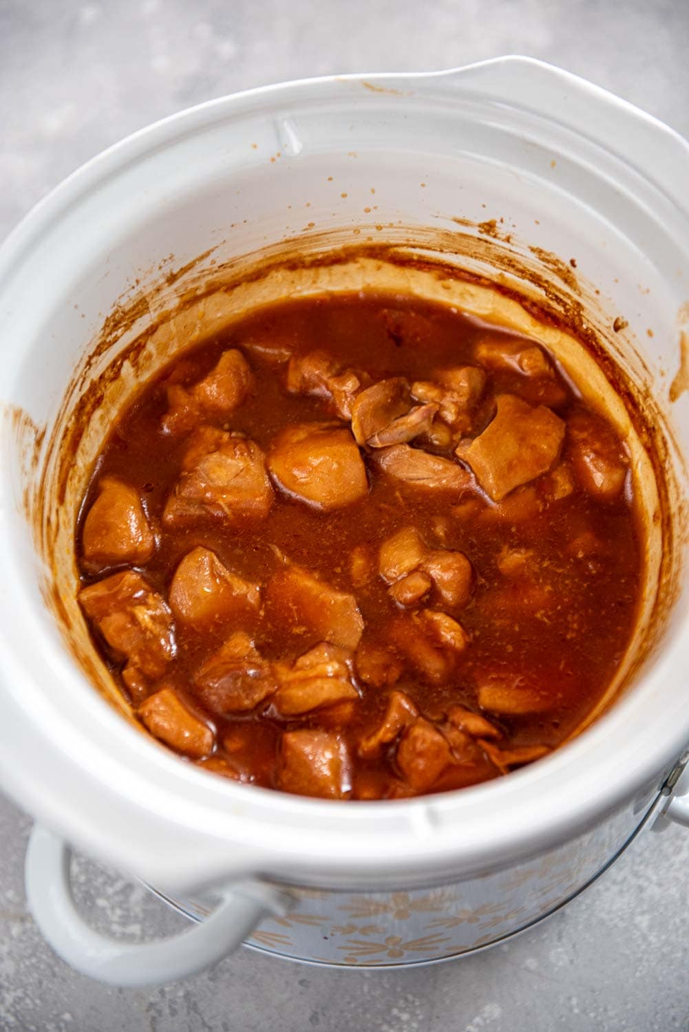 Cooked diced chicken in sauce mixture inside of slow cooker