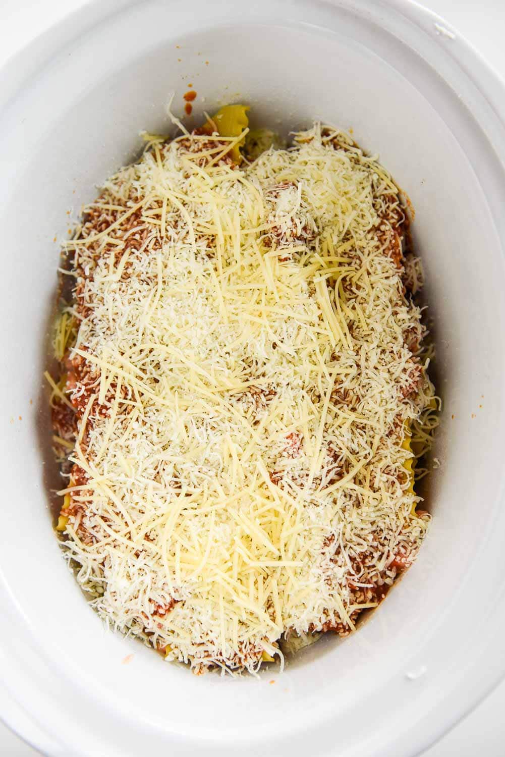 lasagna layers topped with cheese ready to cook in slow cooker
